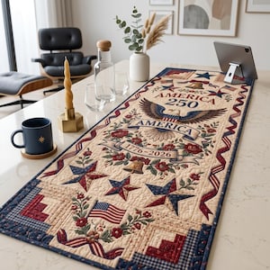 May include: A rectangular quilted table runner featuring a cream background with patriotic motifs including a central bald eagle, the text AMERICA 250, the years 1776-2026, red roses, blue stars, and American flags with a dark blue border trim.