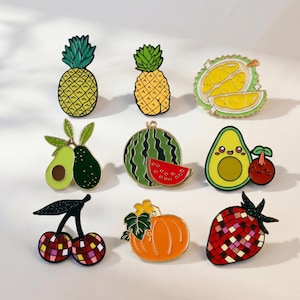 May include: A collection of nine fruit-themed enamel pins featuring a pineapple, durian, avocado, watermelon, cherry, pumpkin, and strawberry. The designs include vibrant colors like yellow, green, red, and orange with various textures and patterns.