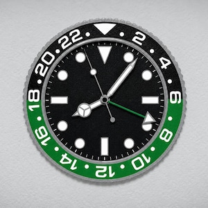 Puede incluir: Un reloj de pared redondo con esfera negra y marcadores de hora circulares y rectangulares blancos. El bisel está dividido en secciones negra y verde con números blancos del 2 al 22. Tiene manecillas blancas y una manecilla GMT de color verde.