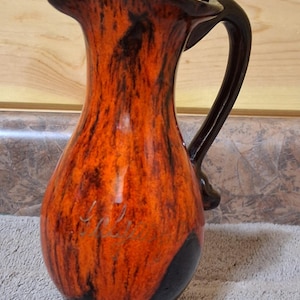 May include: A white ceramic mug with a black handle and the text "But First, Coffee" in a bold, black font. The mug is set against a blurred background, suggesting a cozy setting.