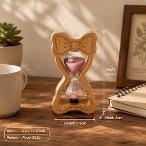 May include: A light-colored wooden hourglass featuring a bow-shaped top frame and pink sand inside the glass bulb. The frame measures 5.3 cm in length, 3 cm in width, and 9.9 cm in height, with a total weight of approximately 62.2 grams.
