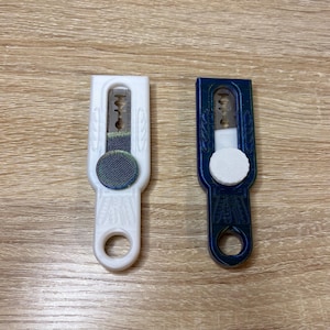 May include: Two utility knives, one white and one dark blue, are displayed side-by-side. Each knife has a blade, a circular button, and a loop at the base. The white knife has a green fabric accent, while the blue knife has a white button.