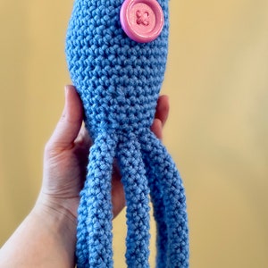 Pu&ograve; includere: Un giocattolo di calamaro all'uncinetto blu con un bottone rosa sulla schiena.