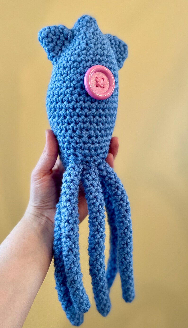Pu&ograve; includere: Un giocattolo di calamaro all'uncinetto blu con un bottone rosa sulla schiena.