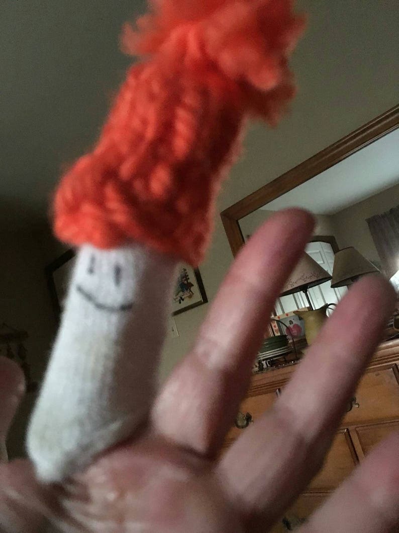 May include: A white finger puppet with a smiling face wearing a bright orange knitted hat.