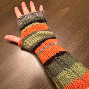 May include: Striped fingerless gloves in orange, green, black, and gray. The gloves are knitted and have a fingerless design.