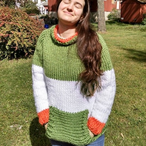 May include: A green, white, and orange striped knitted sweater with a turtleneck and a pocket on the front.
