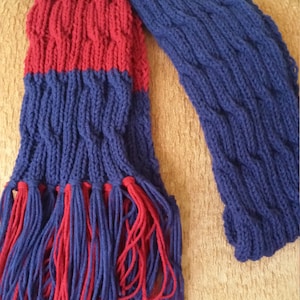 May include: A blue and red knitted scarf with fringe. The scarf has a cable knit pattern.