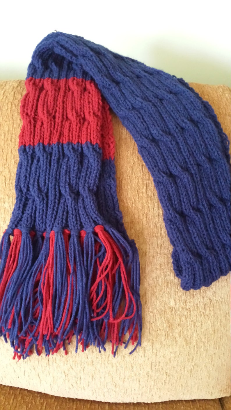 May include: A blue and red knitted scarf with fringe. The scarf has a cable knit pattern.