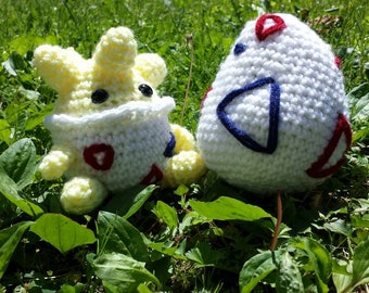 May include: Two crocheted plushies in the shape of Pokemon eggs. The first plush is yellow with white and red details. The second plush is white with blue and red details.