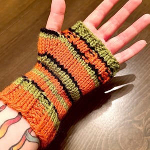 Pode incluir: Luvas sem dedos listradas em laranja, verde e preto, tricotadas em ponto texturizado.