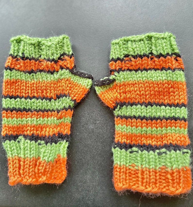 Pode incluir: Um par de luvas sem dedos de cor verde, laranja e preto listradas. As luvas s&atilde;o tricotadas e t&ecirc;m uma textura canelada.