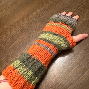 May include: Striped knitted fingerless gloves in orange, green, and gray. The gloves are made with a chunky yarn and have a simple, classic design.