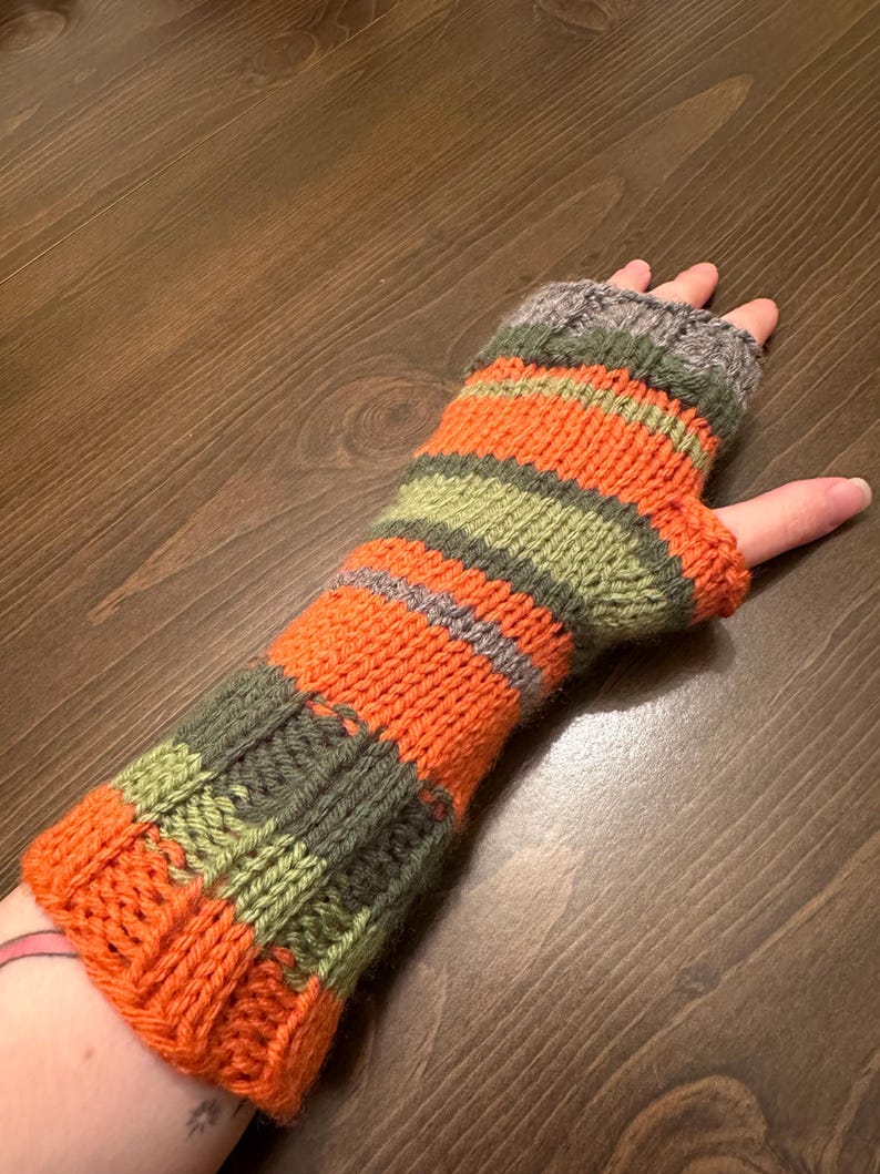 May include: Striped knitted fingerless gloves in orange, green, and gray. The gloves are made with a chunky yarn and have a simple, classic design.