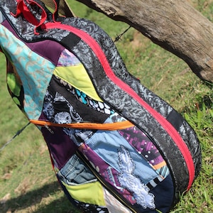 Może przedstawiać: Kolorowy, patchworkowy futerał na gitarę z czarną podstawą i czerwonym zamkiem błyskawicznym. Futerał wykonany jest z różnych tkanin, w tym denimu, wzorów kwiatowych i geometrycznych.