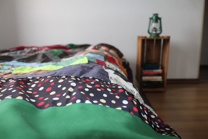 Może przedstawiać: Kolorowa kołdra patchworkowa z zielonym, czarnym i białym wzorem w kropki na dolnym brzegu. Kołdra leży na ł&oacute;żku w pokoju z drewnianą szafką nocną i zieloną latarnią.