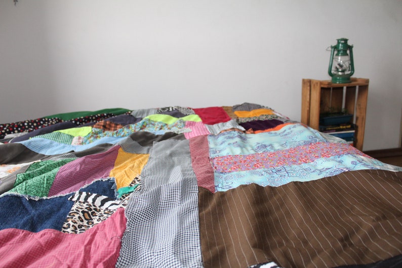 Może przedstawiać: Kolorowa kołdra patchworkowa wykonana z r&oacute;żnych tkanin i wzor&oacute;w. Kołdra składa się z kwadrat&oacute;w i prostokąt&oacute;w w r&oacute;żnych kolorach, w tym zielonym, niebieskim, czerwonym, ż&oacute;łtym i brązowym. Kołdra jest złożona i położona na ł&oacute;żku.