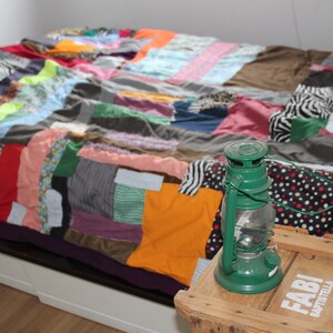 Może przedstawiać: Kolorowa kołdra w patchwork z zieloną latarnią na drewnianym stole z napisem "Fabi" i "B&auml;ckerei".