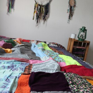 Może przedstawiać: Kolorowa kołdra patchworkowa wykonana z r&oacute;żnych tkanin i wzor&oacute;w. Kołdra składa się z kwadrat&oacute;w i prostokąt&oacute;w w r&oacute;żnych kolorach, w tym czerwonym, niebieskim, zielonym, ż&oacute;łtym i pomarańczowym. Kołdra leży na ł&oacute;żku i jest częściowo złożona.