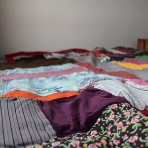 Może przedstawiać: Kolorowa kołdra patchworkowa wykonana z r&oacute;żnych tkanin, z r&oacute;żnymi wzorami i kolorami, w tym szarym, fioletowym, pomarańczowym i niebieskim.