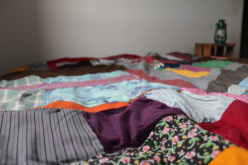 Może przedstawiać: Kolorowa kołdra patchworkowa wykonana z r&oacute;żnych tkanin, z r&oacute;żnymi wzorami i kolorami, w tym szarym, fioletowym, pomarańczowym i niebieskim.