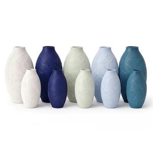May include: A collection of ceramic vases in various sizes and colors. The vases are in white, navy blue, pale green, and light blue. Each vase has a textured leaf pattern. The vases are arranged in a group, showcasing their different shapes and hues.