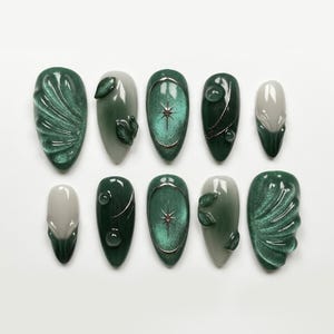 May include: A collection of ten artificial nails in shades of green and grey. Designs include leaf accents, water droplets, and starburst patterns. Some nails have a textured, swirled effect. Measurements are not applicable.