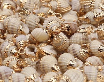 May include: A collection of small, natural off-white spiral seashells, each fitted with a shiny gold-toned metal cap and a small circular jump ring at the top. The shells feature textured ridges and are arranged in a dense, overlapping cluster.