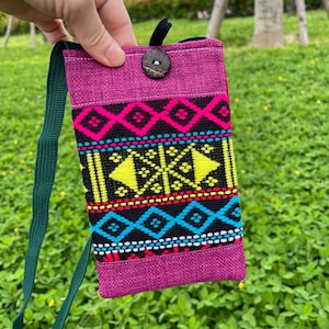 May include: A magenta fabric crossbody bag with a green strap. The bag features a colourful geometric pattern in black, yellow, pink, and blue. A wooden button secures the top flap.