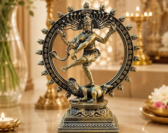 May include: A metallic bronze-toned statue of the deity Shiva Nataraja performing a cosmic dance within a circular ring of flames, standing atop a small figure on a square base, with the text DivijaSacredArt printed at the bottom centre.