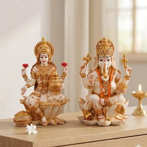 May include: Two ornate statues of Hindu deities, Lakshmi and Ganesha, are presented. Lakshmi, with a golden crown and lotus flowers, sits on a lotus. Ganesha, with an elephant head, sits on a lotus, wearing a garland.