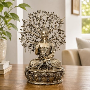 Puede incluir: Una estatua de Buda en tono dorado metálico en posición de loto sentada, con un intrincado fondo de árbol con hojas y ramas detalladas. La figura descansa sobre una base circular adornada con patrones tallados y un acabado texturizado.