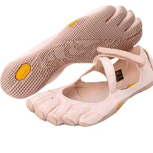 May include: A pair of light pink five-toe shoes featuring individual toe compartments and a textured rubber sole with a yellow Vibram logo. The shoes include a hook-and-loop strap across the top for secure fastening and a flexible, low-profile design.