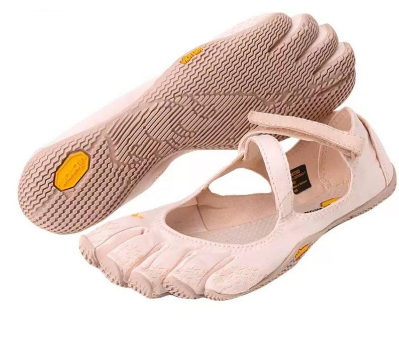 May include: A pair of light pink five-toe shoes featuring individual toe compartments and a textured rubber sole with a yellow Vibram logo. The shoes include a hook-and-loop strap across the top for secure fastening and a flexible, low-profile design.
