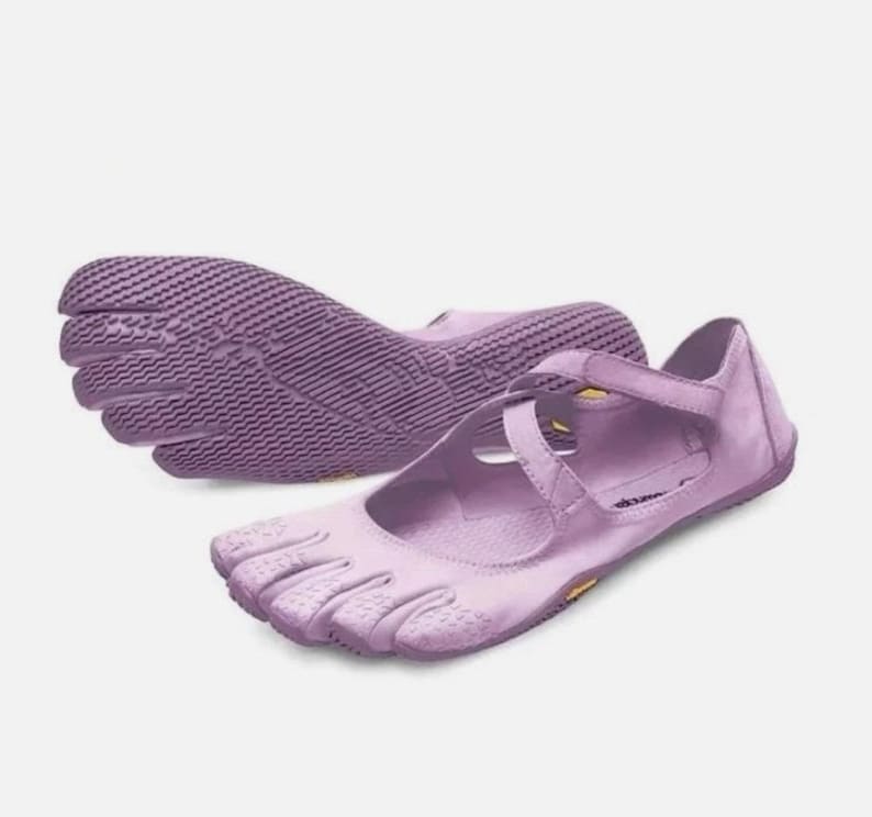 May include: A pair of light purple five-toe shoes featuring a Mary Jane style strap across the top. The shoes have a textured, flexible sole with individual toe compartments and a smooth upper material, showcasing a distinct minimalist design.