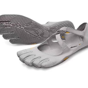 May include: A pair of light gray five-toe shoes featuring individual toe compartments, a textured rubber sole, and crisscross straps across the top. The shoes include small yellow Vibram logos on the side and the sole, with a low-profile design.