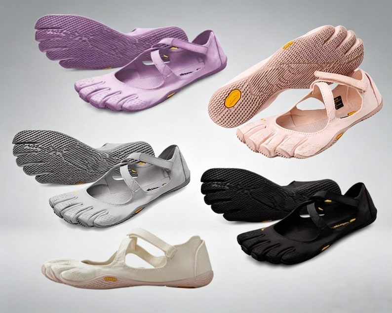 May include: A collection of five-toe shoes in purple, light pink, gray, black, and off-white. Each shoe features a flexible rubber sole with a textured grip pattern, individual toe compartments, and a cross-strap closure across the top of the foot.
