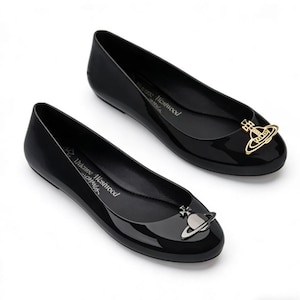 Puede incluir: Un par de bailarinas negras brillantes. Cada zapato presenta un emblema decorativo en la puntera. El nombre de la marca "Vivienne Westwood" está impreso en el lateral. Las bailarinas tienen una puntera redondeada y un tacón bajo.