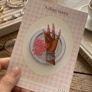 May include: A pink and white checkered card with the text "A clingy bunny" and a graphic of a hand with long nails, a watch, and bracelets. The card also has the text "Clock That Tea".
