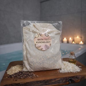 Könnte beinhalten: Ein klarer Plastikbeutel mit einem beigefarbenen Badetee-Sachet mit dem Text "BATH TEA KUSCHELZEIT" auf einem runden Etikett. Der Beutel liegt auf einem Holzbrett mit verstreuten Körnern und einer kleinen Glasflasche. Im Hintergrund eine Badewanne und brennende Kerzen.