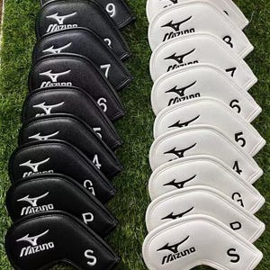 Puede incluir: Un conjunto de fundas para palos de golf en blanco y negro. Las fundas están etiquetadas con números y letras, incluyendo "S", "P" y "G". Cada funda presenta el logotipo "Mizuno".