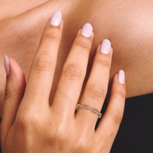 May include: A gold-colored chain link ring with small, clear stones set in the links. The ring is worn on a finger, with the hand and arm visible. The nails are painted a light pink color.