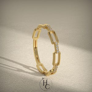 May include: A gold ring with a chain link design. The ring features rectangular links connected in a continuous loop. Small, clear gemstones are set in the links. The ring is displayed on a neutral background.