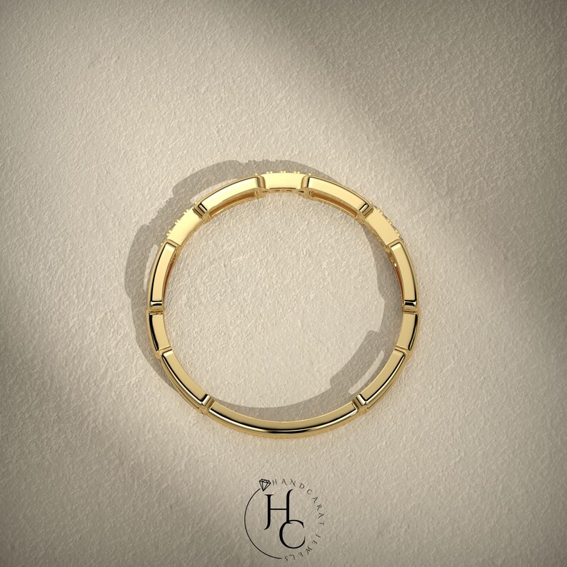 May include: A top-down view of a gold ring with a rectangular design. The ring is made of gold and has a series of rectangular segments around the band. The ring is set against a neutral background.