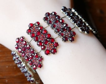 May include: A red garnet bracelet with multiple rows of small, faceted stones set in silver-toned metal.