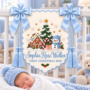 Könnte beinhalten: Ein cremefarbener Wandbehang mit gewelltem Rand, der ein Lebkuchenhaus, einen Weihnachtsbaum und einen Schneemann zeigt. Der Text lautet Sophia Rose Walker FIRST CHRISTMAS 2026. Verziert mit zwei hellblauen Satinschleifen und Quasten.