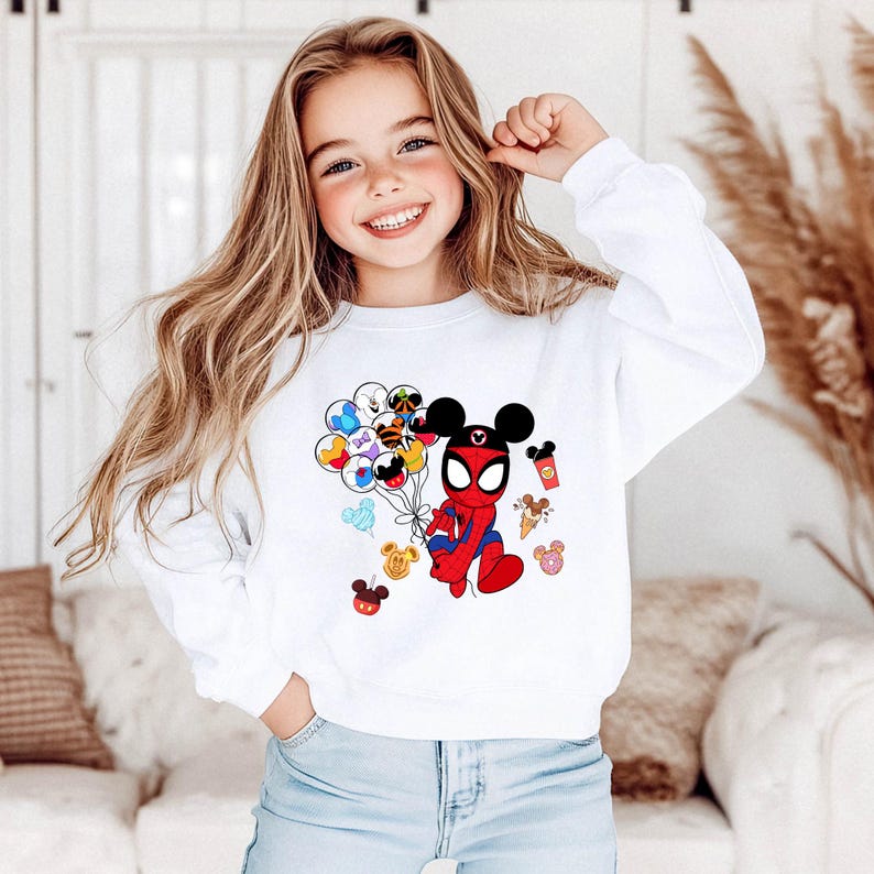 May include: White sweatshirt featuring a cartoon illustration of a hybrid Spider-Man and Mickey Mouse character holding balloons. The design includes Mickey Mouse ears, a Spider-Man suit, and various Disney-themed icons.