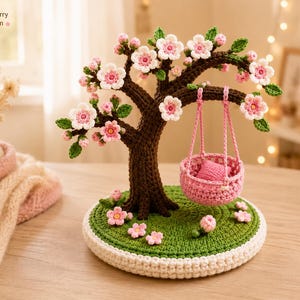 May include: A handcrafted crochet tree with pink and white blossoms and green leaves. A small pink swing hangs from a branch. The tree sits on a green base with white trim, and the text "Krosh Cherry blossom" is in the upper left corner.