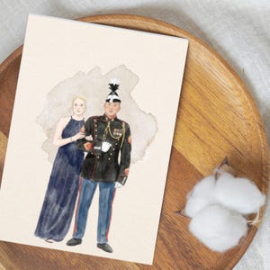 Op de afbeelding: Een aquarelillustratie op een rechthoekige kaart met een persoon in een donkerblauwe avondjurk naast een persoon in een zwart militair uniform met een blauwe broek, een witte hoed met een zwarte pluim en gouden accenten.