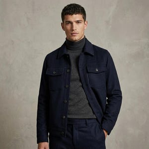 May include: A dark navy blue button-up jacket with two chest pockets and a pointed collar, worn over a charcoal grey turtleneck sweater. The jacket features a structured design with visible buttons down the front and on the pocket flaps.